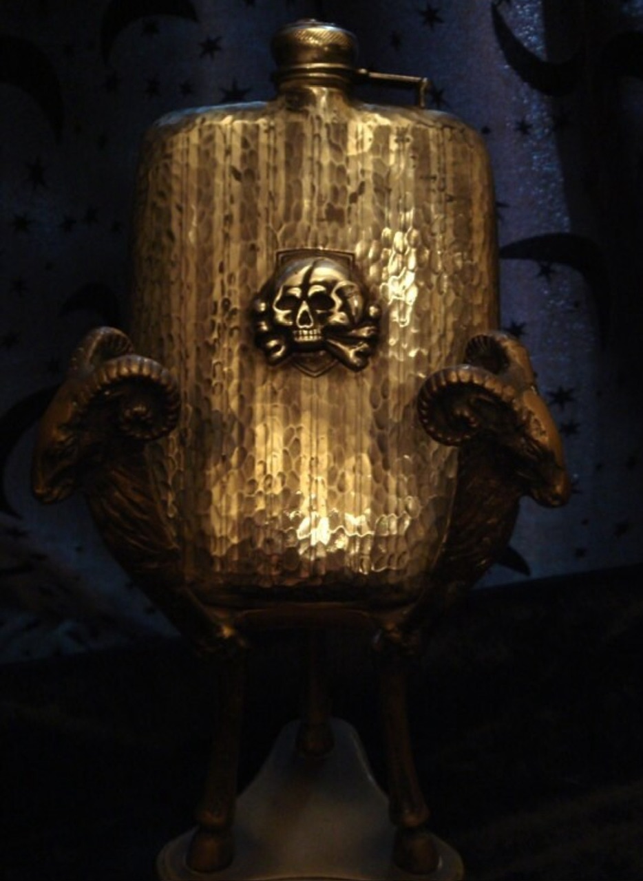 「骷髅骨」Vintage Skull Flask·一个古旧的、不寻常的弧形烧瓶·酒壶·水壶；正面和盖子上有头骨和交叉骨浮雕印章；它像锤子银一样闪闪发光，未尝试过抛光或清洁它，可能是锡，找到的唯一标记是P.C.C.C.和STYLO MADE IN AMERICA（斯泰洛美国制造）；6英寸x 3 3/4英寸宽；被告知这是20世纪60或70年代的；山羊座台不包含在内；哥特风（20141208）