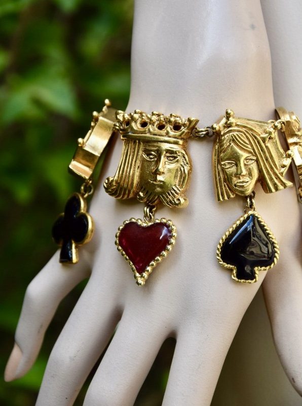 ②.国王王后侍从·头像扑克牌主题IC手链；华美且极为罕见的Isabel Canovas作品，出自“Les Jeux”系列（1991年冬季）。以扑克牌中的国王、王后与侍从头像为主题，每一枚皆配有对应的浇铸玻璃符号吊饰：红与黑两色，分别对应红心、方块与梅花、黑桃，隐含情感、财富、行动与命运的象征，构思巧妙而富有趣味。链条搭配龙虾扣闭合。背面刻有签名。镀金；法国制造IC7681