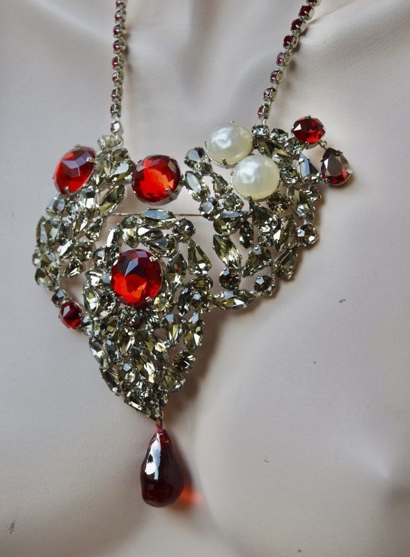 ②.传奇爱心设计·收藏级YSL胸针短项链；圣罗兰（Yves Saint Laurent）的标志性作品，诞生于20世纪60年代，最初仅制作了3件（分别收藏于品牌档案馆、大都会艺术博物馆以及私人收藏中）。该设计几乎出现在每一季高级定制秀中，并在多年间不断被重新演绎，配以红色水晶链条，亦推出更小尺寸版本。此件为大尺寸高级定制作品，镶嵌烟色水晶、红色玻璃弧面宝石（cabochon）与珍珠，底部垂有红色吊坠；配有一条可拆卸的红色水晶链，可作为短项链佩戴或作为胸针使用。背面带有品牌签名。合金/人造水晶珍珠等；法国制造90年代YSL10675