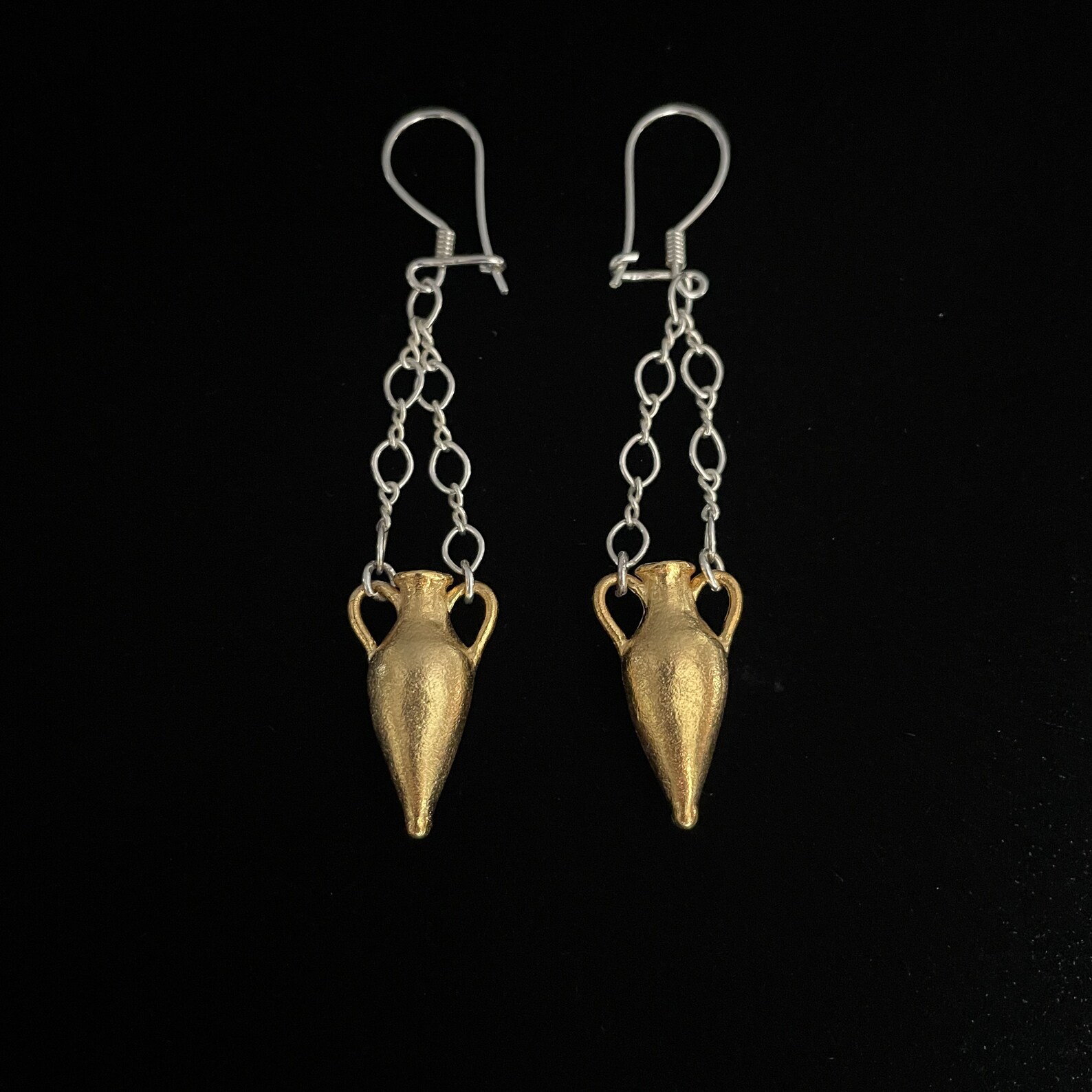 ②.双耳瓶·”考古”系列·耳环；土耳其手艺人Göksu作品；灵感源自古希腊与古罗马陶器。双耳瓶承载着储存、运输与日常使用的功能，也象征古典文明延续至今的物质痕迹。通过缩小尺度、器身中空以减轻重量，同时保留厚度与质感，使其既具雕塑感，又化身为可佩戴的古典意象。镀金黄铜+925纯银；瓶子约2.2cm，每只约7g；加上链条和耳钩总长约7cm（可依需求缩短）。古老失蜡法，纯手工雕刻制作｜x4426