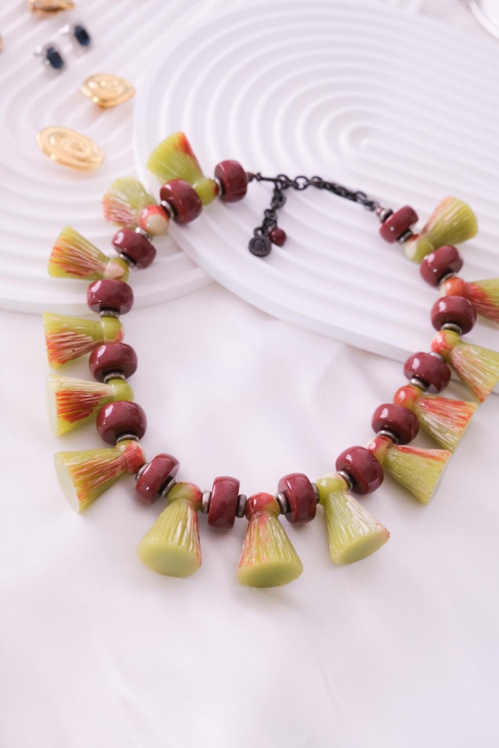 ②.复古日式风情树叶流苏植物形态GA短项链；Giorgio Armani（乔治·阿玛尼）；标志性黑化金属链条之下垂落一组淡绿色树脂植杆截面构件，间以酒红色珠饰，富有节奏的排列；造型接近流苏与植物形态的转译，既有装饰性，也保留结构的清晰感。背部带品牌签名，附原盒；约49厘米；黑化金属/树脂；1980年代法国制造