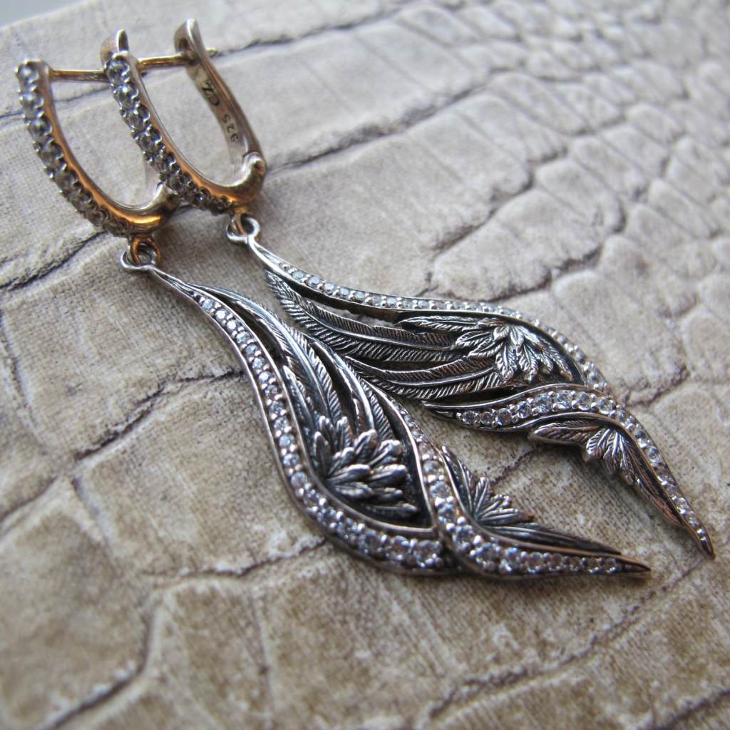 ②.天使之翼·装饰艺术风格垂坠SK耳环，90年代泰国制作；925纯银打造，镶嵌锆石。线条呈展开的羽翼形态，轻盈下垂，在细微的摆动中呈现柔和光泽。整体结构简洁而优雅，带有一丝古典气息。背面带有设计师签名及925银标记。925纯银/锆石（CZ: cubic zirconia）；约5.5cm×1.1cm；藏于美国