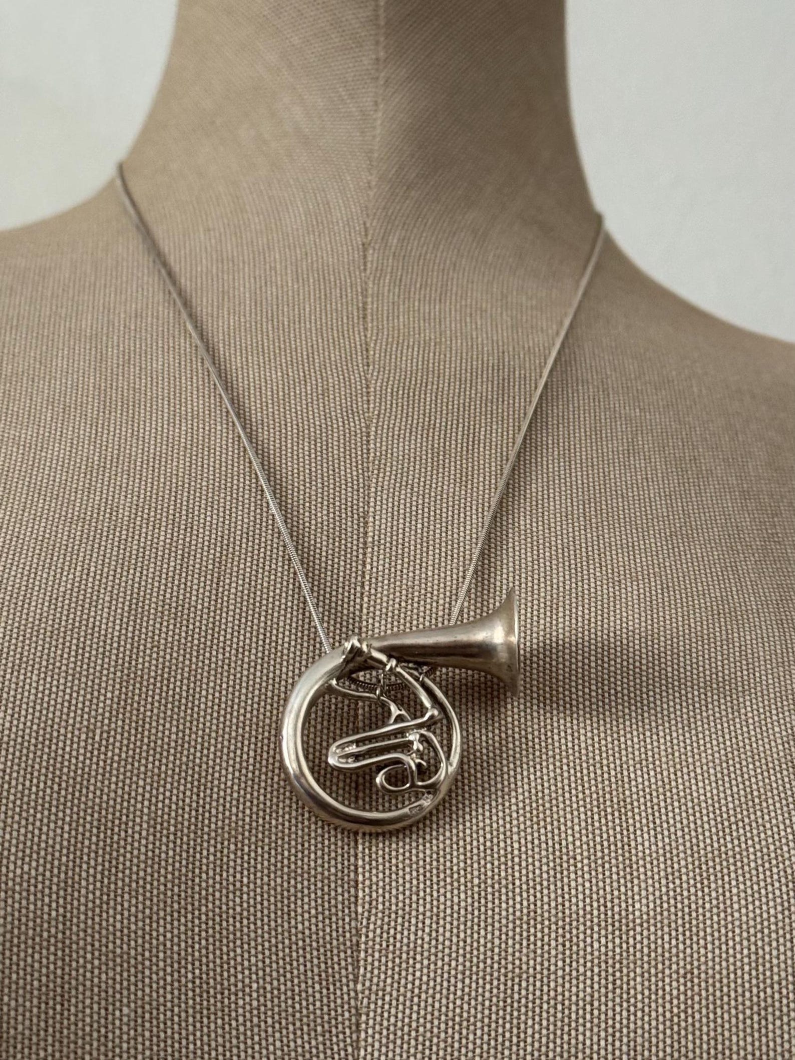 ②.法国号·音乐交响乐器项坠项链；以法国号为形，线条回旋流动，构成优雅而克制的轮廓。整体抛光处理，使金属在光线中呈现柔和光泽。乐器的形态被转译为佩戴之物，在装饰之外，隐约带有声音与节奏的联想。925纯银，约3.2×4cm，链长约61cm，90年代制作；西班牙｜x6626