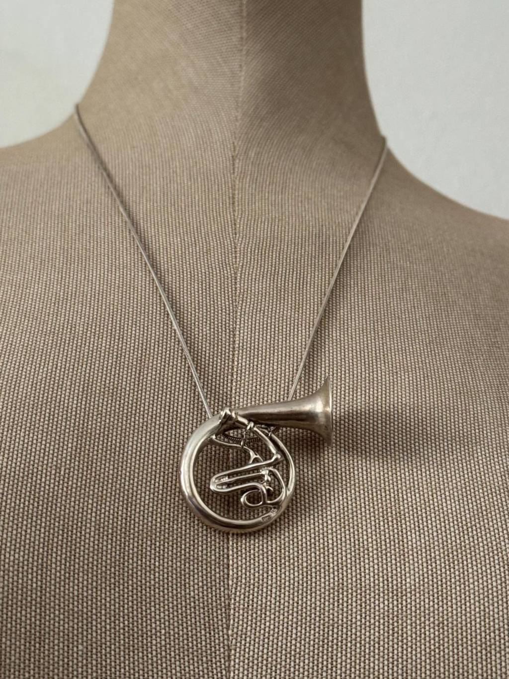 ②.法国号·音乐交响乐器项坠项链；以法国号为形，线条回旋流动，构成优雅而克制的轮廓。整体抛光处理，使金属在光线中呈现柔和光泽。乐器的形态被转译为佩戴之物，在装饰之外，隐约带有声音与节奏的联想。925纯银，约3.2×4cm，链长约61cm，90年代制作；西班牙