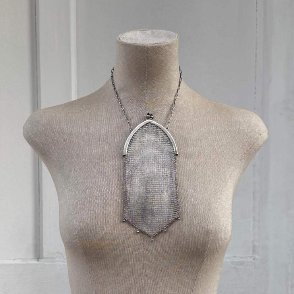 ②.经典ArtDeco网状晚宴1920s锁子甲手袋；细密编织的金属网身自然垂落，下缘呈尖形轮廓，并点缀小珠流苏。弧形金属框配以深蓝色圆拱琉璃宝石扣饰，在冷调金属中形成克制的色彩对比。网状结构随动作产生柔和流动与光泽变化，保留了20世纪初晚宴配饰特有的轻盈与精致。附原链条。手袋约18×9cm，链长约33cm，德国银/琉璃，1920年代制作；完好无损；西班牙