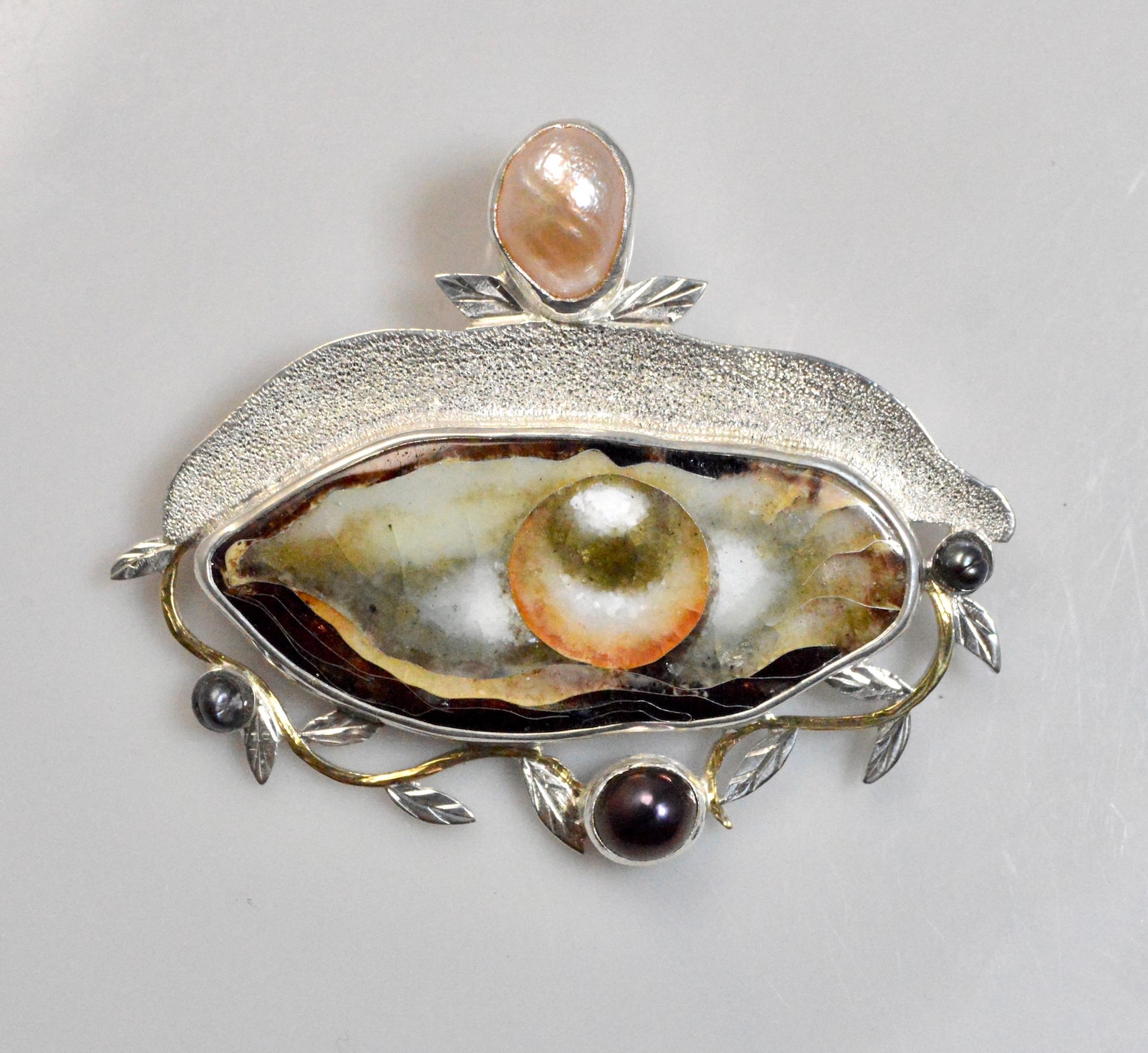 ②.「生成&孕育」贝壳珍珠意象·项坠吊坠；格鲁吉亚手艺人Natia作品；贝壳外壳以珐琅呈现，色彩层次丰富；内部呈现一颗夸张比例的珍珠，形成强烈的视觉对比。金粉色与黑色珍珠点缀其间，使整体在光泽与质感上产生变化。隐藏式挂环设计，使造型更完整。景泰蓝珐琅/925纯银/淡水珍珠，约5.5×4.5cm；前锋艺术，像一只眼睛，也让人想到维纳斯的诞生…；孤独品｜x6826