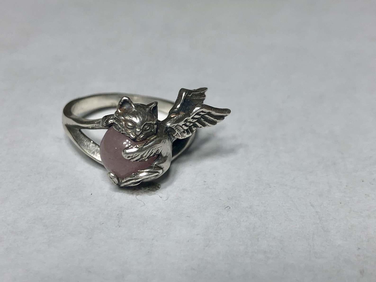 ②.天使猫咪怀抱宝石·童话气息·戒指环；美国手艺人Natia作品；「微小而重大的陪伴」；小猫镶嵌圆形宝石，由四足与下巴托着，背部展开双翼，造型轻盈而完整。结构贴合手指，保留细节的同时兼顾佩戴舒适度。925纯银/天然宝石（图为玫瑰石英/粉晶，亦有多种宝石可选）；定制尺码。古老失蜡法纯手工制作｜x7226