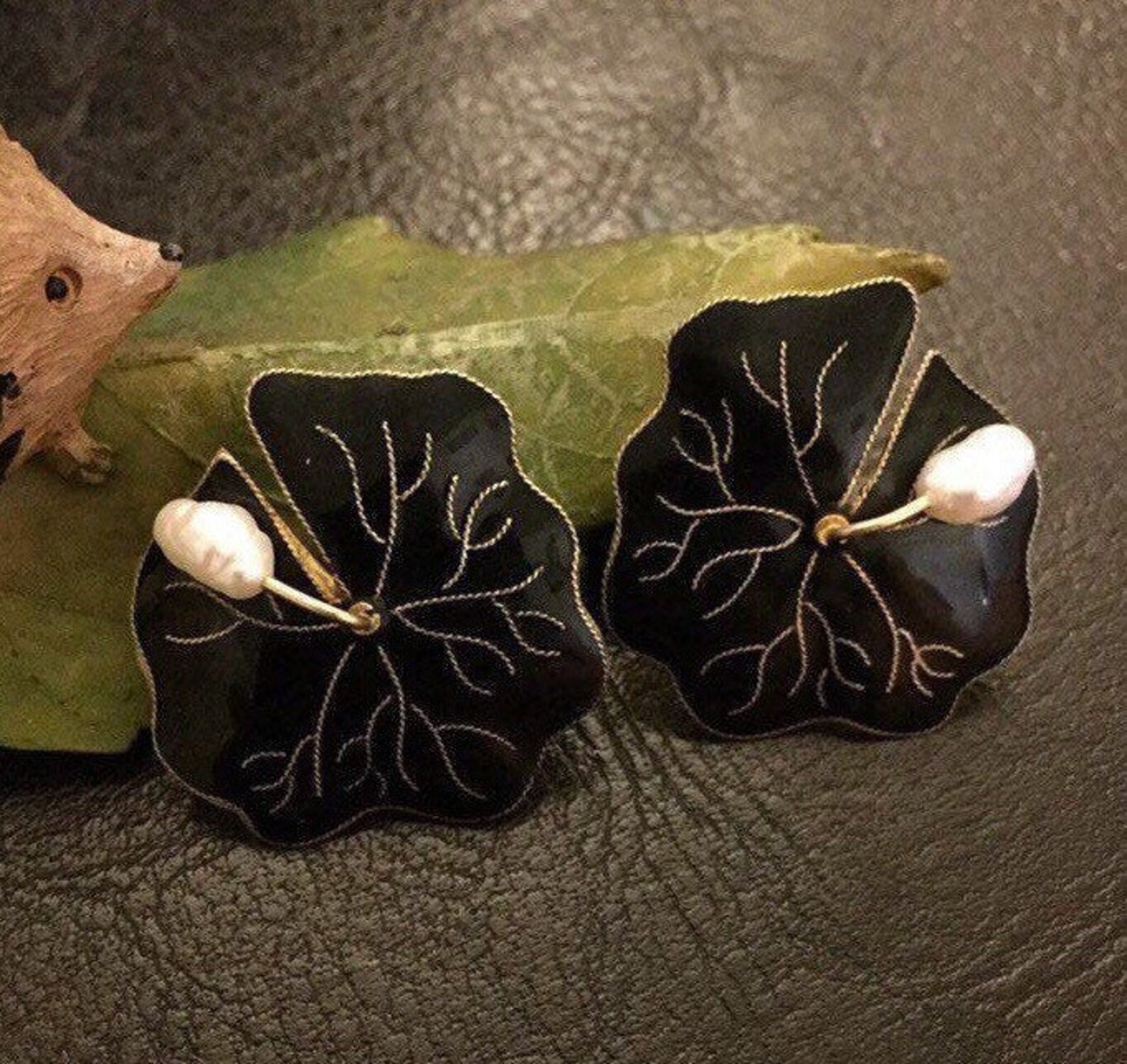 ②.睡莲耳环；Art Deco+自然主义；以不规则的睡莲为形，花瓣呈平面缓缓展开，黑色珐琅构成沉静而集中的色面，中央点缀弯垂的巴洛克异型白色珍珠，形成优雅且柔和的对比。整体结构对称规整中带着略随意慵懒的气息，色彩与比例克制。睡莲常与水面相关：「安静、平展，呈现一种不被打扰的存在方式」。背面标记925；重约6.7g；直径约2.5cm；925纯银镀金/珐琅/淡水珍珠；美国｜x8526