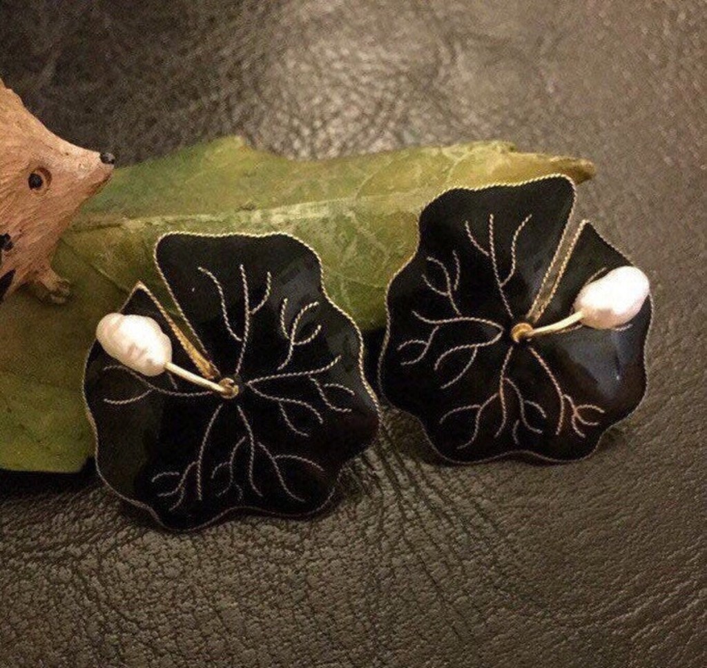 ②.睡莲耳环；Art Deco+自然主义；以不规则的睡莲为形，花瓣呈平面缓缓展开，黑色珐琅构成沉静而集中的色面，中央点缀弯垂的巴洛克异型白色珍珠，形成优雅且柔和的对比。整体结构对称规整中带着略随意慵懒的气息，色彩与比例克制。睡莲常与水面相关：「安静、平展，呈现一种不被打扰的存在方式」。背面标记925；重约6.7g；直径约2.5cm；925纯银镀金/珐琅/淡水珍珠；美国