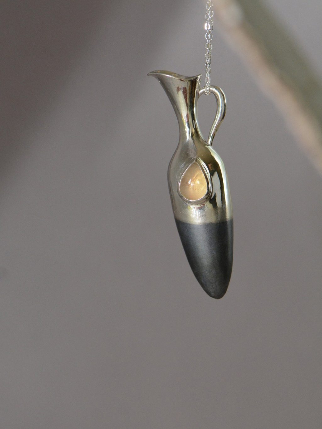 ②.「仍然感受和珍视」泪瓶项链；以色列手艺人Irina作品；新艺术+现代主义；这枚泪瓶将无形的悲伤凝固成形。不论是美人鱼之泪、天使之泪，还是人之泪，都在那宝石里闪烁微光。哀愁是生命经验的一部分；承认生活的荒谬，是走向力量与自我的前提。细长瓶身呈垂直延展形态，表面结合哑光与抛光质感；半部哑光处理氧化黑色银质的瓶身象征沉静，宝石如”泪滴般”清晰。925纯银/淡黄色拉长石或欧泊（可选）；项坠约5×1.2cm；有刻字服务｜x8626