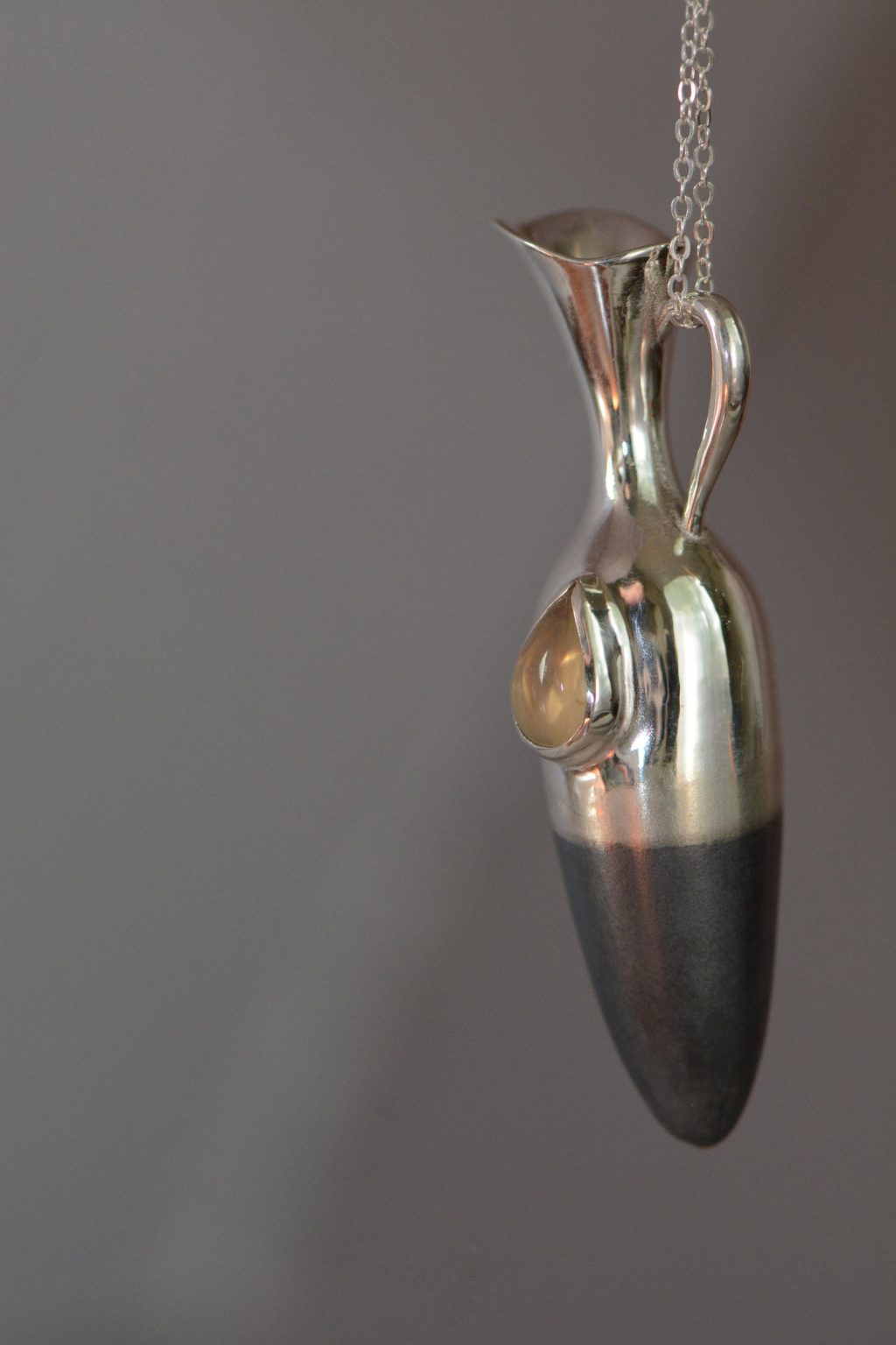 ②.「依然活着、感受和珍视」泪瓶项链；以色列手艺人Irina作品；这枚泪瓶将无形的悲伤凝固成形。不论是美人鱼的泪、天使的泪，还是凡人的泪，都在那宝石里闪烁微光。哀愁是生命经验的一部分；承认生活的荒谬，是走向力量与自我的前提。细长瓶身呈垂直延展形态，表面结合哑光与抛光质感；半部哑光处理氧化黑色银质的瓶身象征沉静，宝石如”泪滴般”清晰。925纯银/淡黄色拉长石或欧泊（可选）；项坠约5×1.2cm；新艺术+现代主义