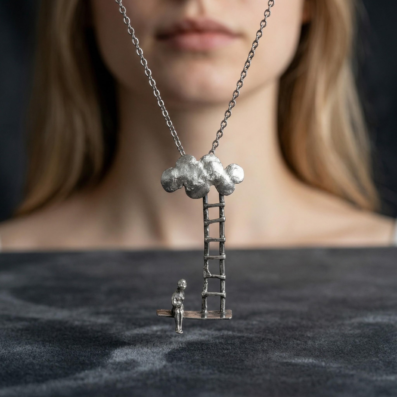 ②.「女人与通天云梯」坐者、梯子与云朵吊坠项链；德国手艺人Noko作品；极简抽象派艺术/现代主义；一个女人侧坐于长凳上，身体微转，目光停留在斜置的天梯上。梯子一端置于凳上，另一端延伸至一朵云。云朵似乎代表着某种抽象形式。于是，梯子便连接了现实与想象，也隔开了行动与停留；它被放置在那里，仿佛已经预设了方向。而她静坐在旁，像在思考、在感受，又或在观察。氧化银的质地让整体更显沉静，手工的细微痕迹，则保留了一种未被修整的素朴与真实。925纯银，约45×20mm，链长约55cm｜x9226